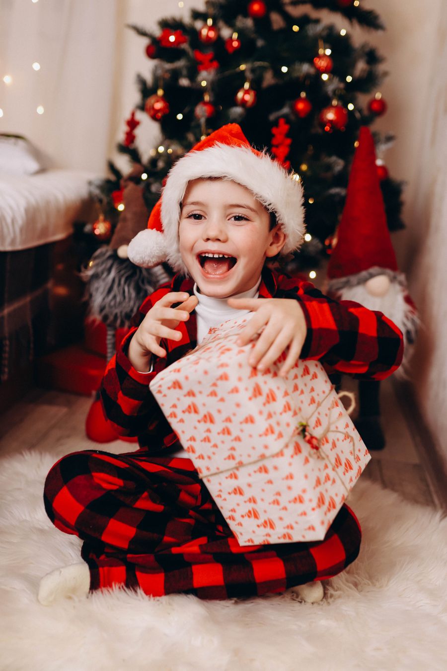 Delighted child in a Santa hat opening a Christmas present by the tree