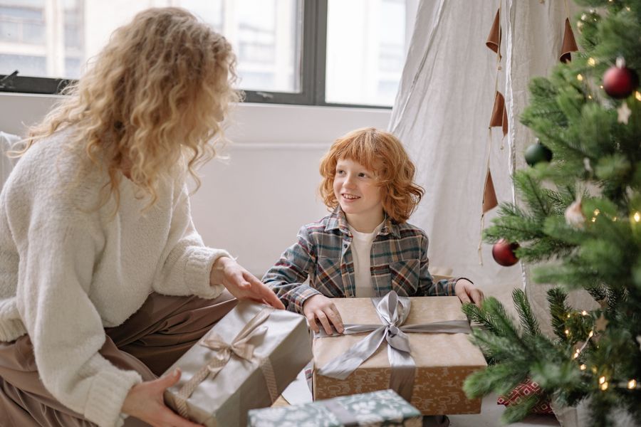 Boy and his mom opening Christmas presents by the tree